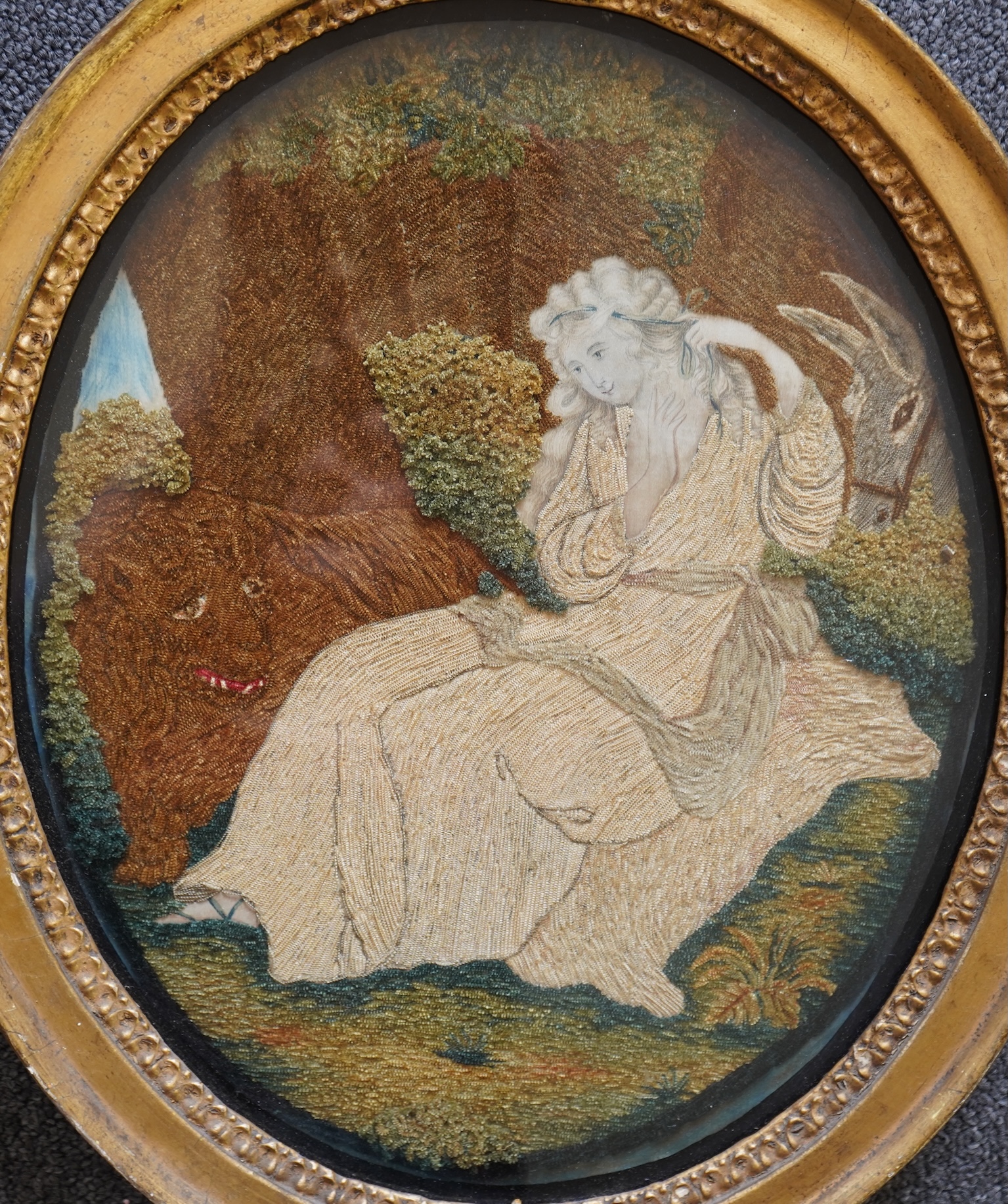 A pair of unusual early 19th century oval silk Chenille embroideries, one depicting a seated lady surrounded by a lion and donkey, the other depicting a seated shepherdess under tree with two sheep. Both have water colou